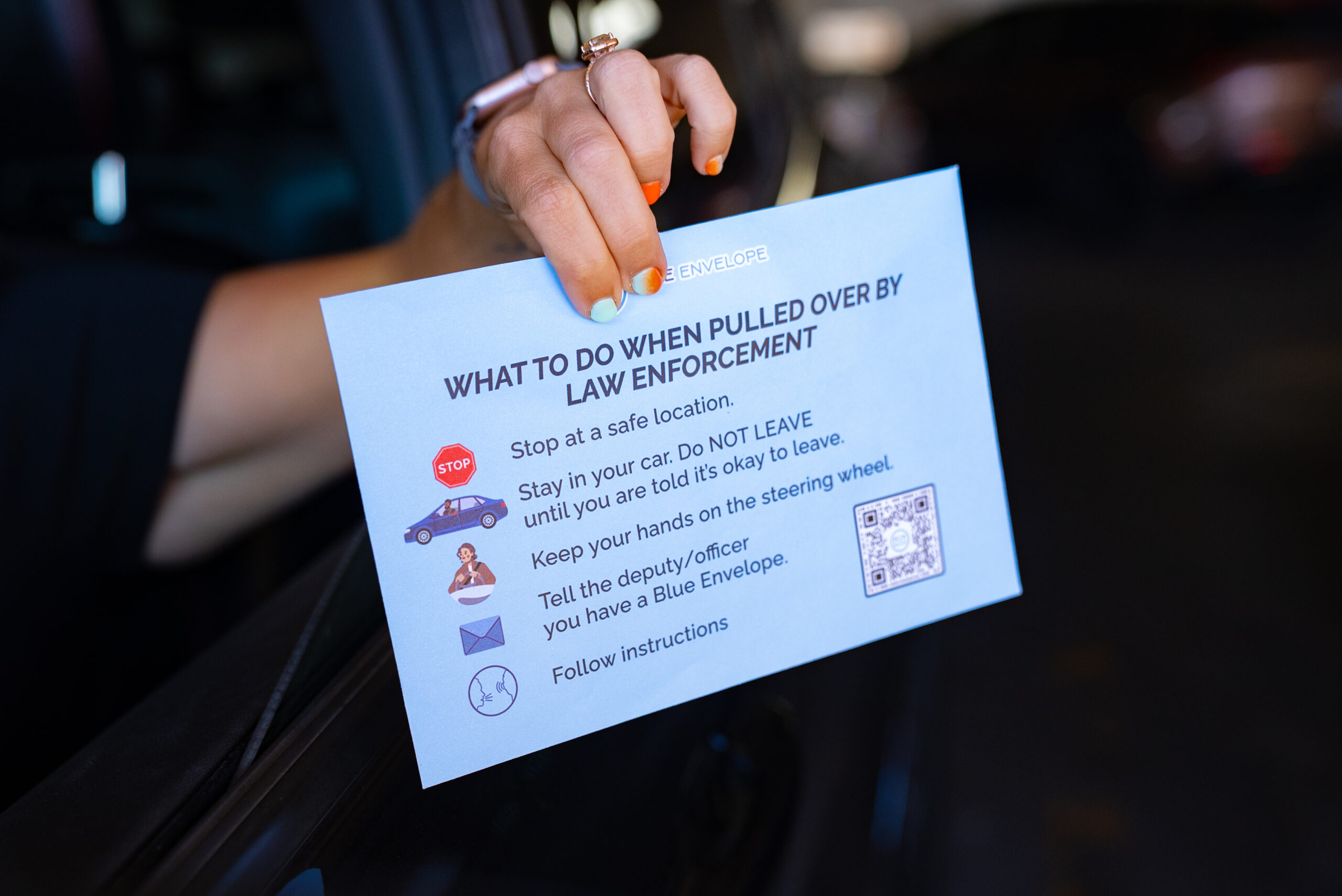 Hand holding a blue envelope out of car window.